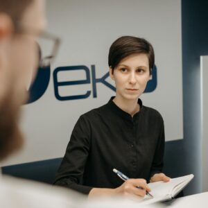 A receptionist at a clinic desk writing notes during a consultation.
